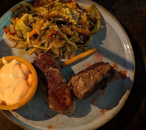 Dos cortes de carne a la plancha con vegetales salteados con sésamo y una salsa aparte